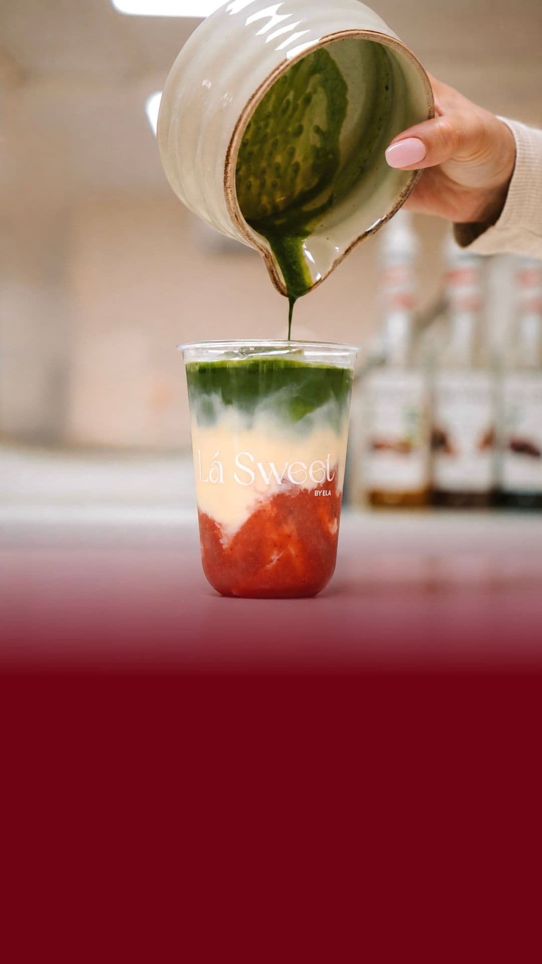 Matcha wordt over aardbei en melk in een Lá Sweet-beker geschonken